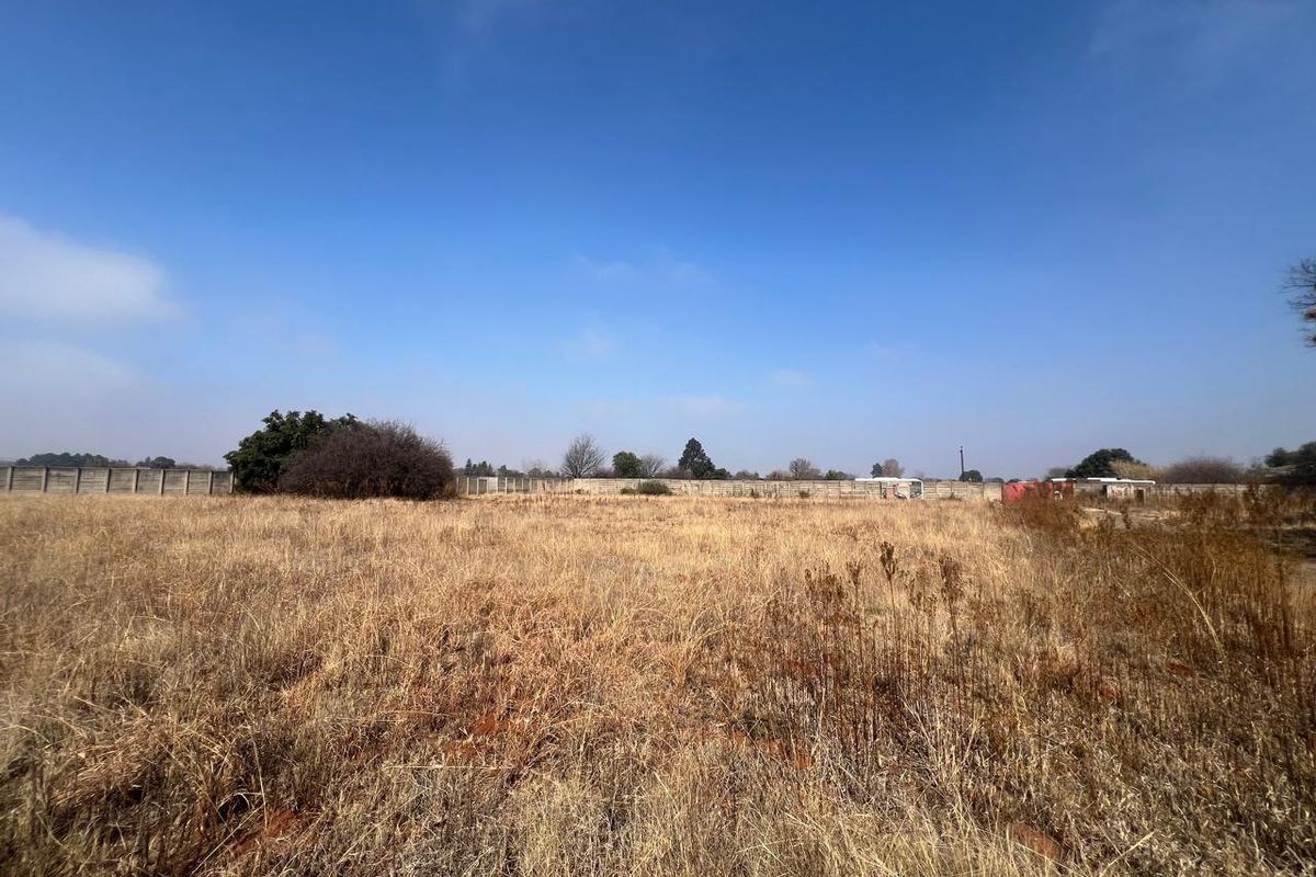 A wide-angle view of a vacant residential plot featuring dry grass and a perimeter boundary wall.