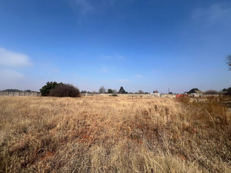 A wide-angle view of a vacant residential plot featuring dry grass and a perimeter boundary wall.