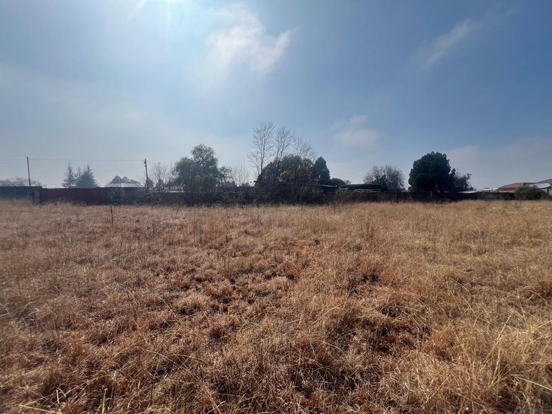 A wide-angle view of a vacant residential plot featuring dry grass and perimeter fencing, offering a blank canvas for future development.
