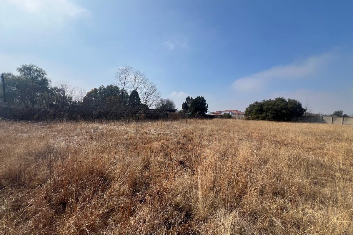 A wide-angle view of a vacant residential plot featuring dry grass and perimeter boundary walls, offering a blank canvas for future development.