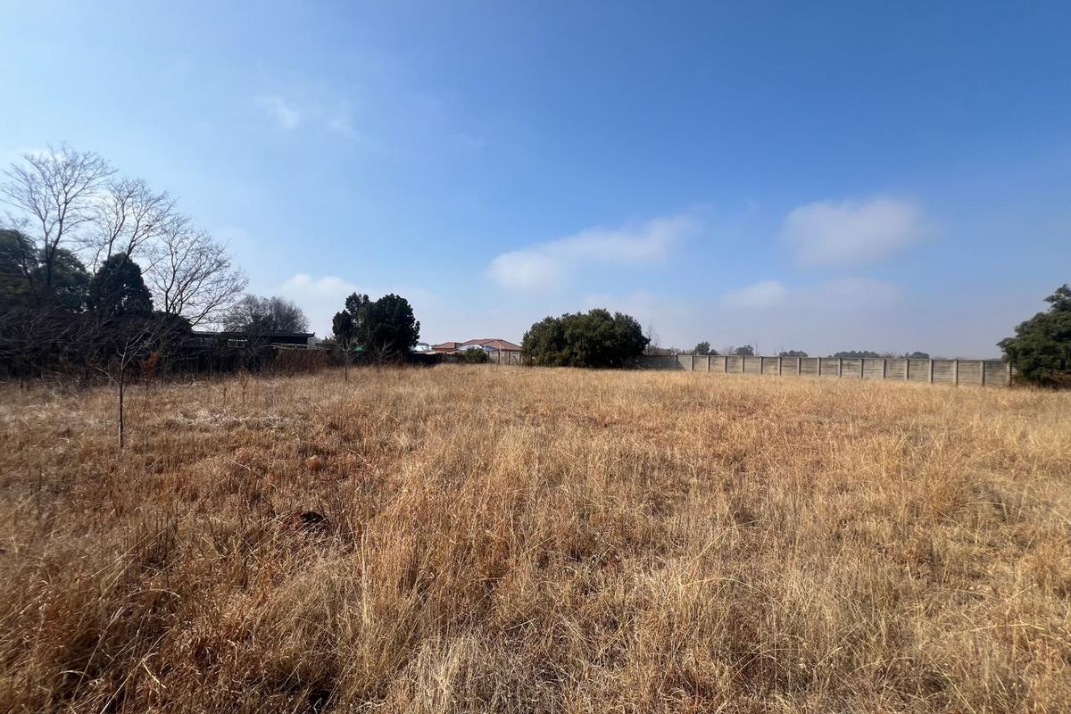 A wide-angle view of a vacant residential plot featuring dry grass and a perimeter boundary wall.