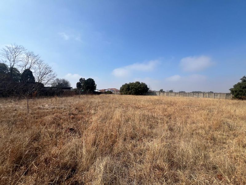 A wide-angle view of a vacant residential plot featuring dry grass and a perimeter boundary wall.