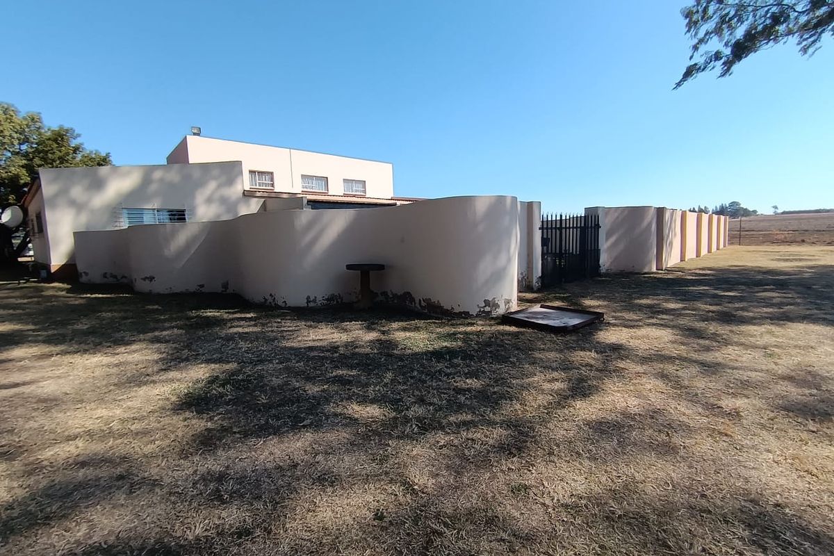 Rear view of the property featuring a curved boundary wall with security gate and security bars on windows.