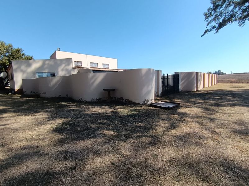 Rear view of the property featuring a curved boundary wall with security gate and security bars on windows.