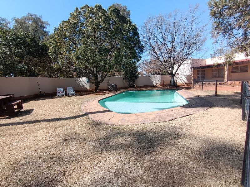 Outdoor pool area featuring a swimming pool with paved surround, enclosed by a perimeter wall and fencing in a spacious garden setting.