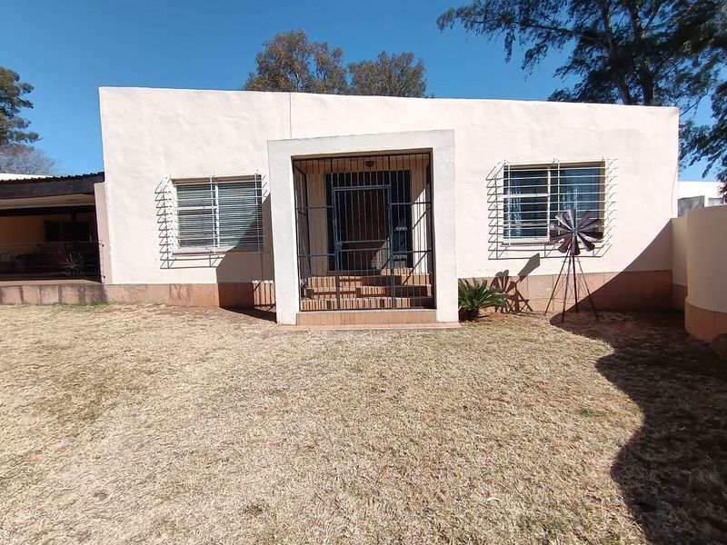 Rear view of a single-story house featuring a plastered facade, tiled entrance steps, and security bars on windows, set against a dry lawn.