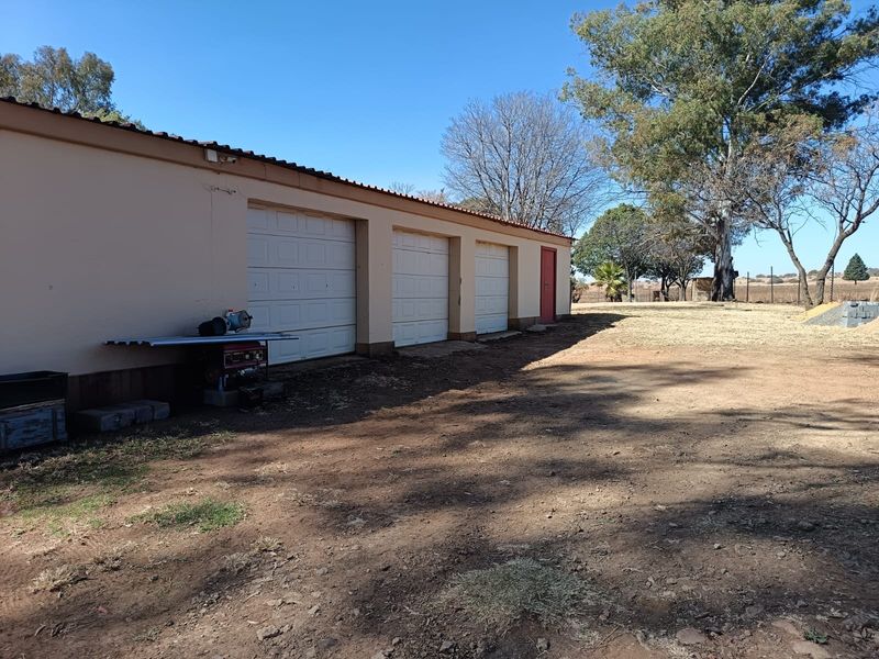 A detached triple garage building with three sectional doors and a side entrance, situated on a large open plot.