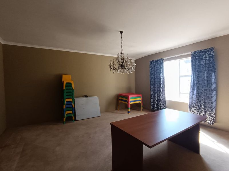 A spacious living area featuring neutral wall tones, carpeted flooring, and an elegant crystal chandelier, offering a versatile space for various interior layouts.