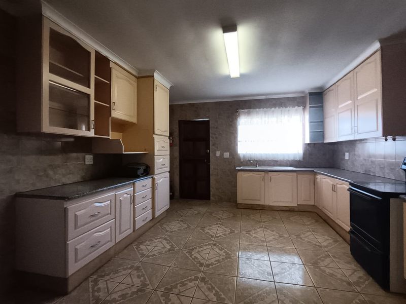 A spacious kitchen featuring fitted cabinetry, granite countertops, tiled flooring, and a built-in oven, offering a functional layout with ample storage space.