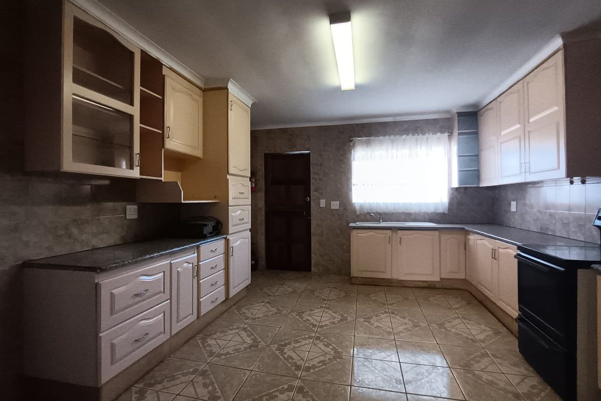 A spacious kitchen featuring fitted cabinetry, granite countertops, tiled flooring, and a built-in oven, offering a functional layout with ample storage space.