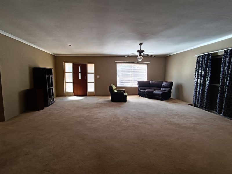 Spacious living room featuring carpeted flooring, a ceiling fan, and natural light through a large window and sliding glass door.