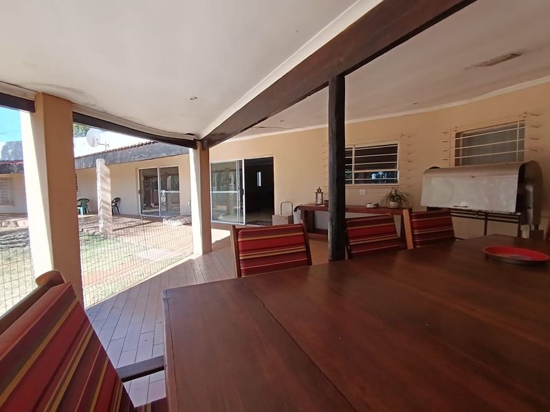 A covered outdoor patio area featuring timber decking, a built-in braai, and direct access to the home through sliding glass doors.