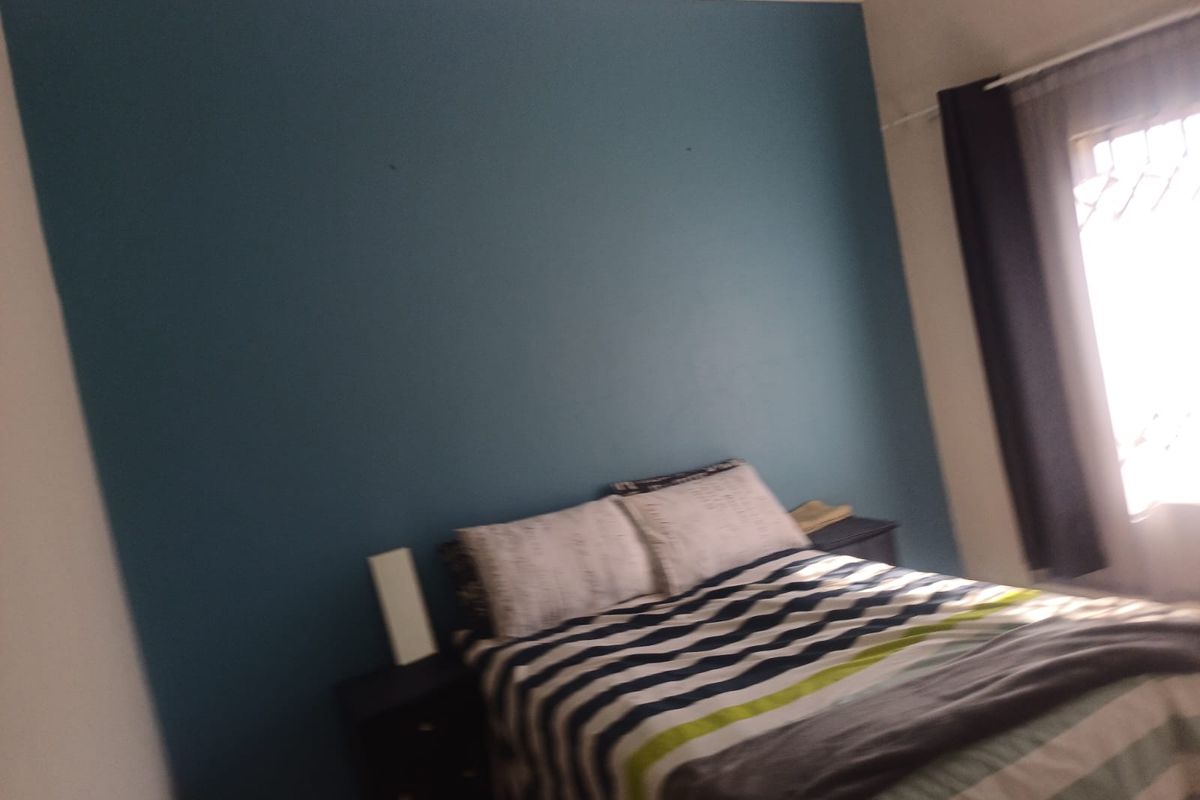 A bedroom featuring a blue accent wall and natural light from a window with curtains.