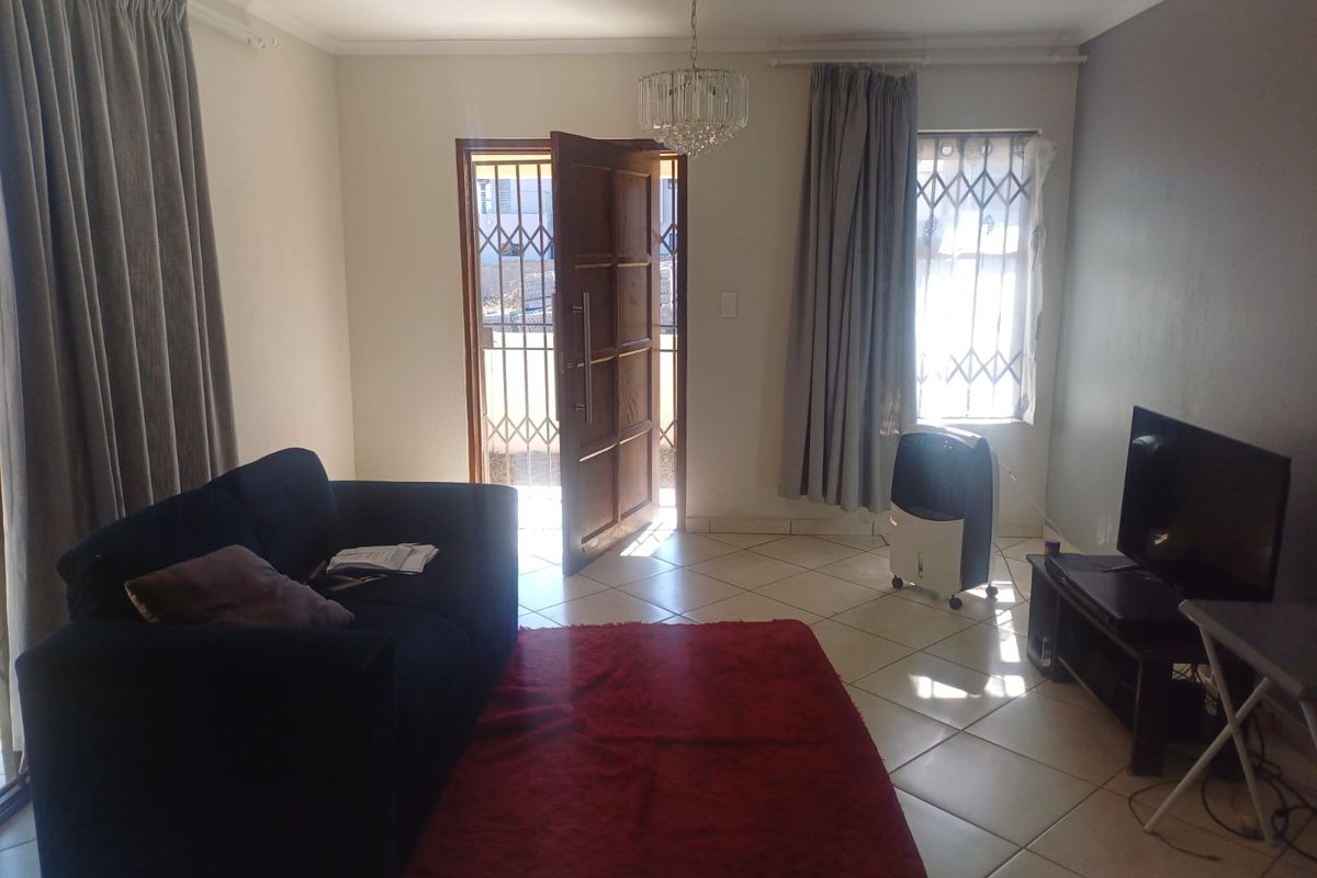 A living room featuring tiled flooring, a decorative chandelier, and a security gate at the entrance door.