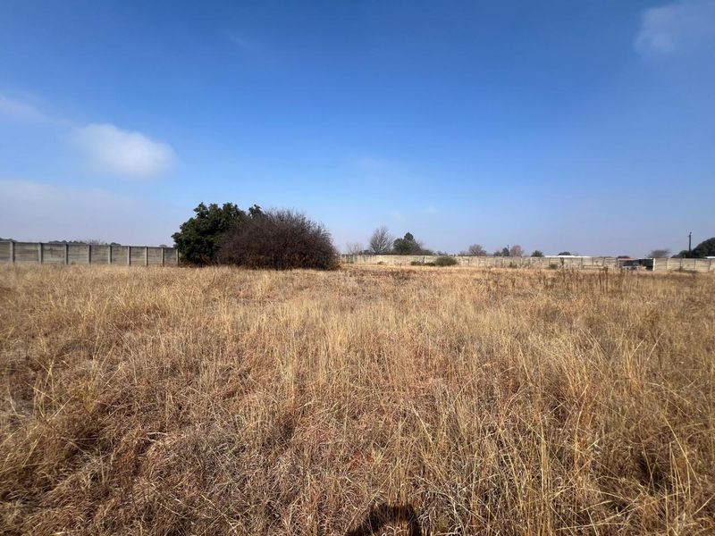 A view of a vacant residential plot featuring dry grass and a precast concrete boundary wall enclosing the property.