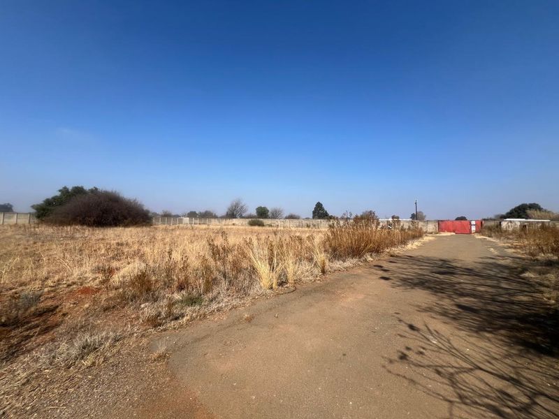 A vacant residential plot featuring a paved driveway, perimeter walling, and a gated entrance, offering a blank canvas for future development.