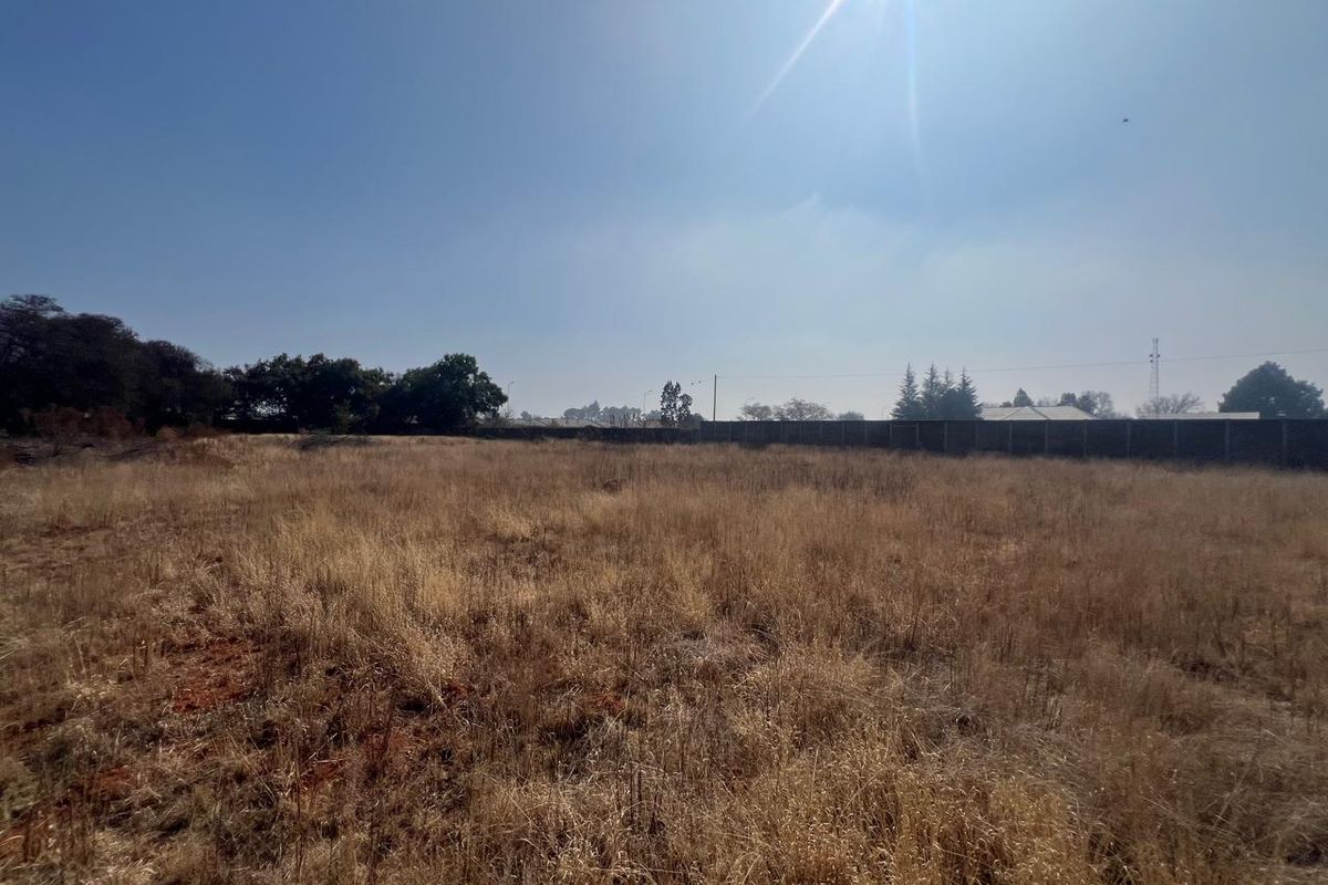 A vacant residential plot featuring dry grass and a perimeter wall, offering a blank canvas for future development.