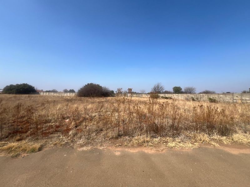 A vacant residential plot featuring dry grass and a precast concrete boundary wall, offering a clear space for future development.