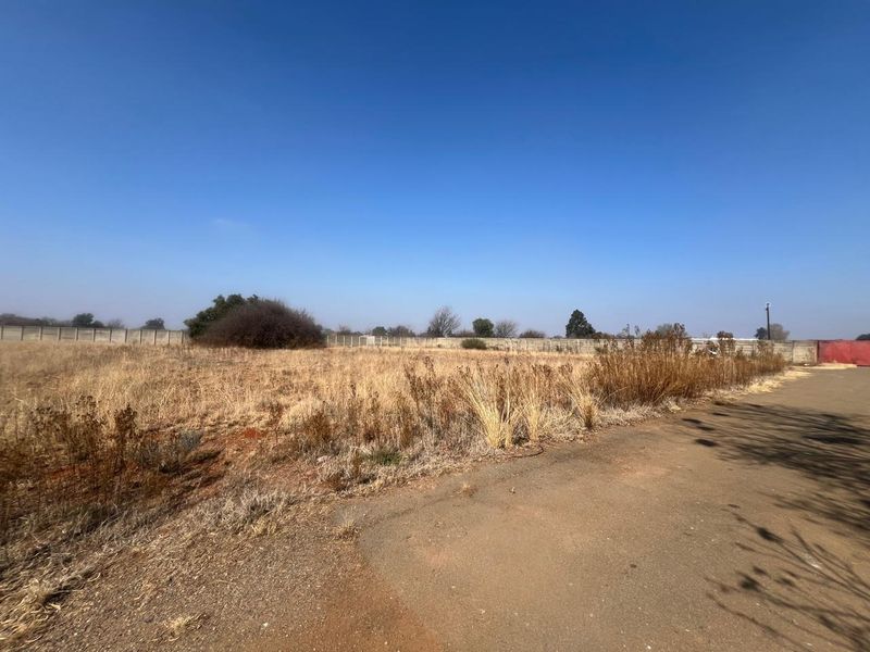 A vacant residential plot featuring a perimeter wall and adjacent paved access road, ready for development.