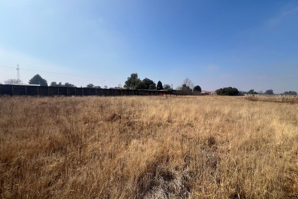 A wide-angle view of a vacant residential plot featuring dry grass and a perimeter boundary wall.