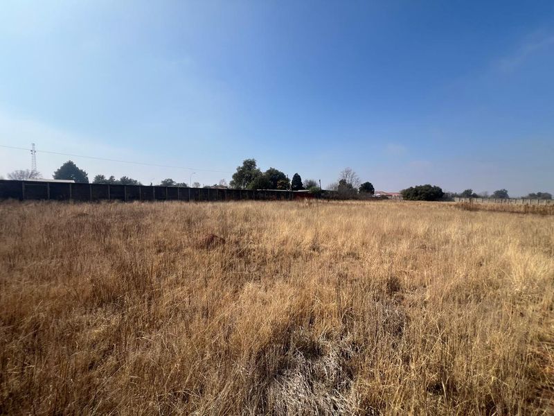 A wide-angle view of a vacant residential plot featuring dry grass and a perimeter boundary wall.