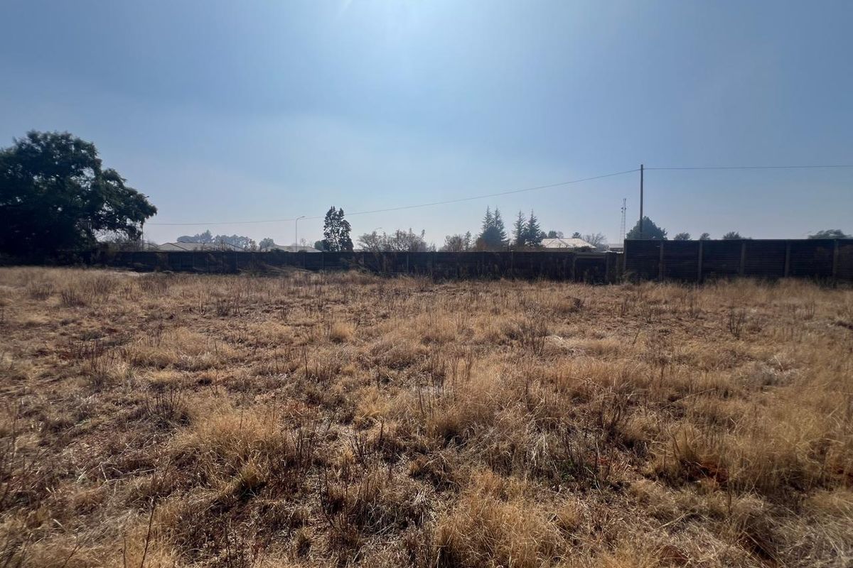 A vacant residential plot featuring dry grass, a perimeter wall, and utility infrastructure, offering a blank canvas for future development.