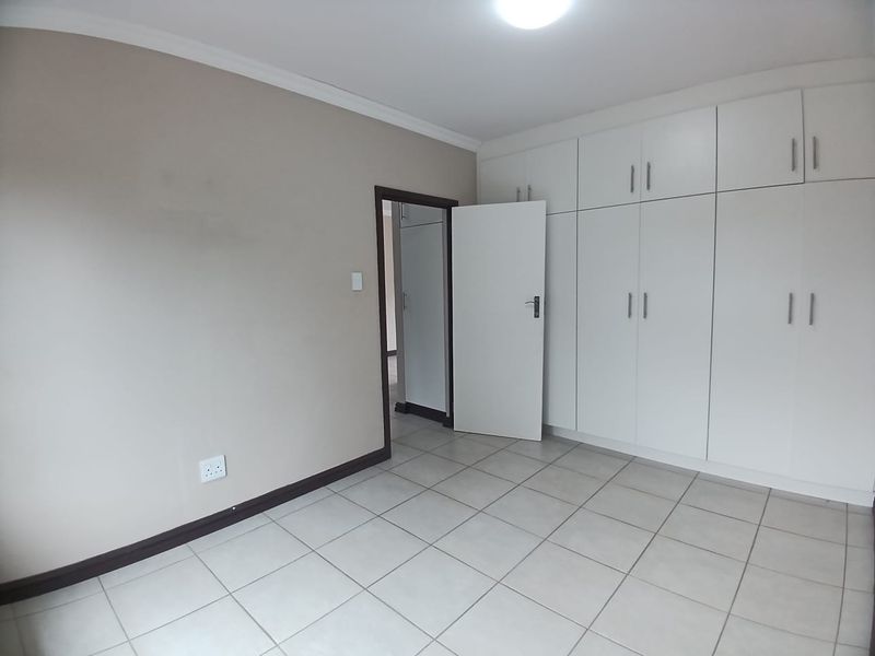 A clean, empty bedroom featuring neutral wall tones, tiled flooring, and extensive white built-in cupboards providing ample storage space.