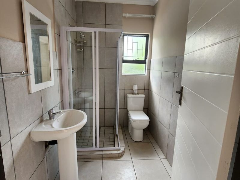 A clean and functional bathroom featuring a pedestal basin, a glass-enclosed shower, and a toilet, finished with neutral wall and floor tiles.