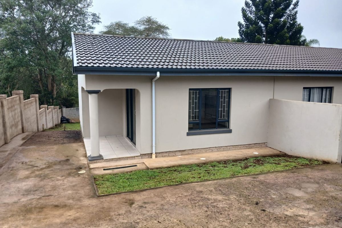 Rear view of the cottage featuring a covered patio, tiled roof, and security-fitted windows, set against a boundary wall with unfinished garden space.