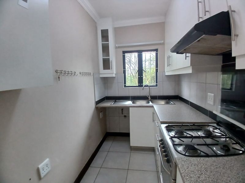 A functional kitchen featuring built-in cabinetry, stone countertops, a gas hob with extractor fan, and a stainless steel sink with tiled splashback.