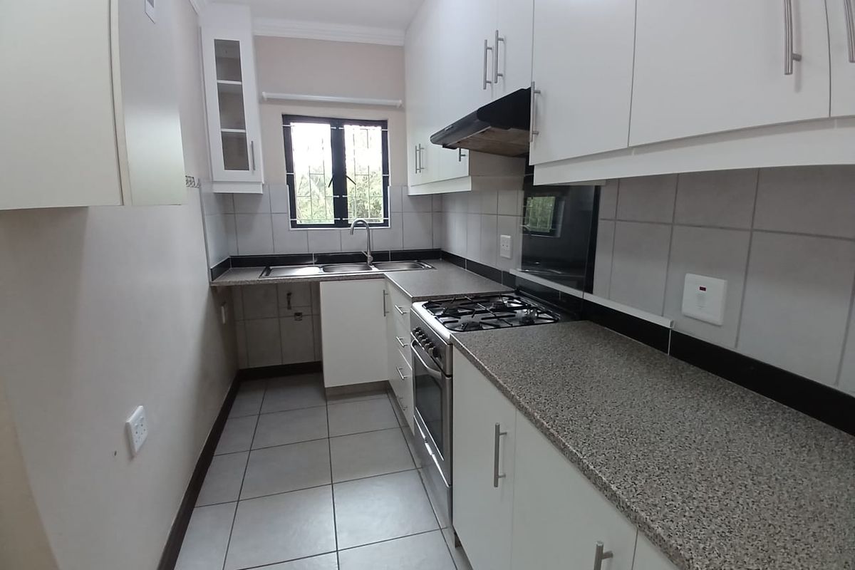 A clean, functional kitchen featuring white cabinetry, granite countertops, a gas hob, and tiled finishes, offering a bright and practical workspace.