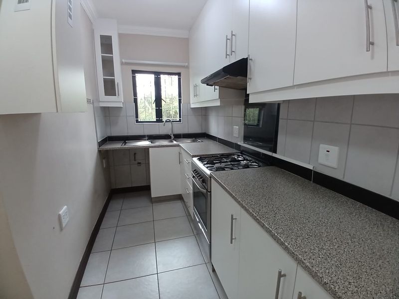 A clean, functional kitchen featuring white cabinetry, granite countertops, a gas hob, and tiled finishes, offering a bright and practical workspace.