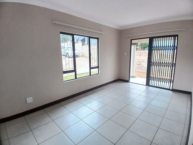 A bright, empty living room featuring neutral tiled flooring, security bars on the windows, and a sliding door leading to an outdoor area.