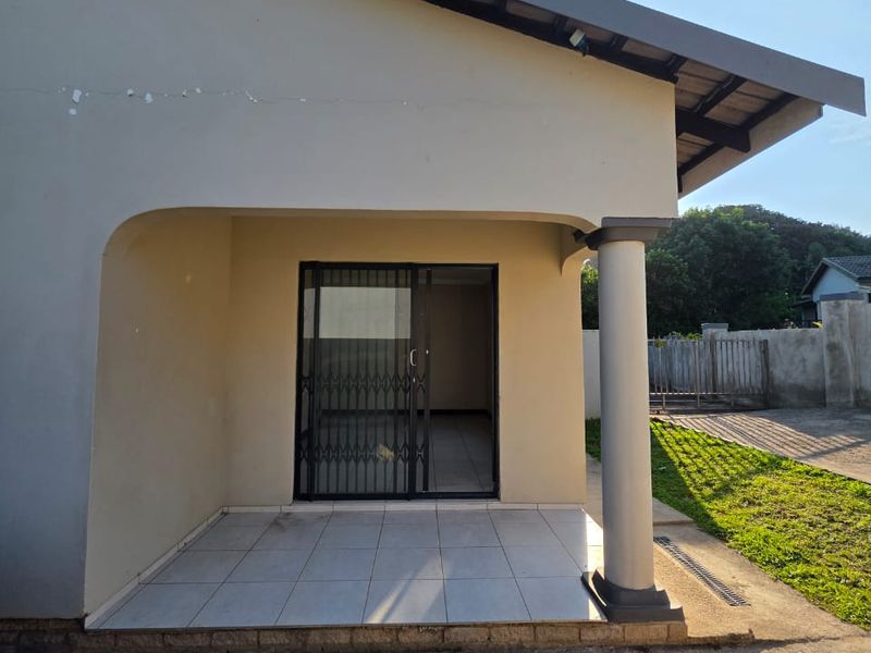 A covered patio area featuring tiled flooring, a sliding glass door with a security gate, and a structural support column.