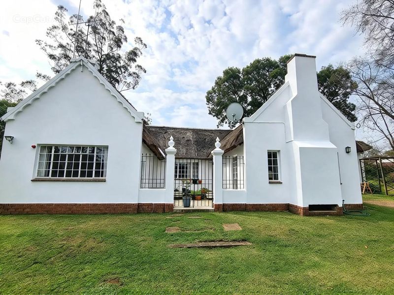 A charming cottage-style home featuring a traditional thatched roof, white rendered walls, brick base detailing, and a central gated entrance.