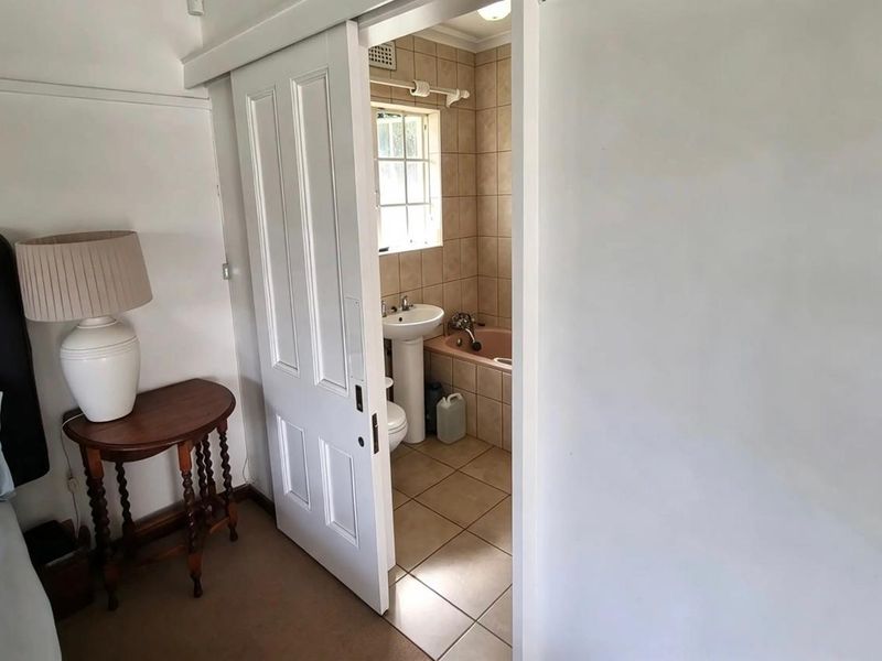A bathroom featuring a pedestal basin, bathtub, and tiled finishes, accessed via a white sliding door from the adjacent bedroom.