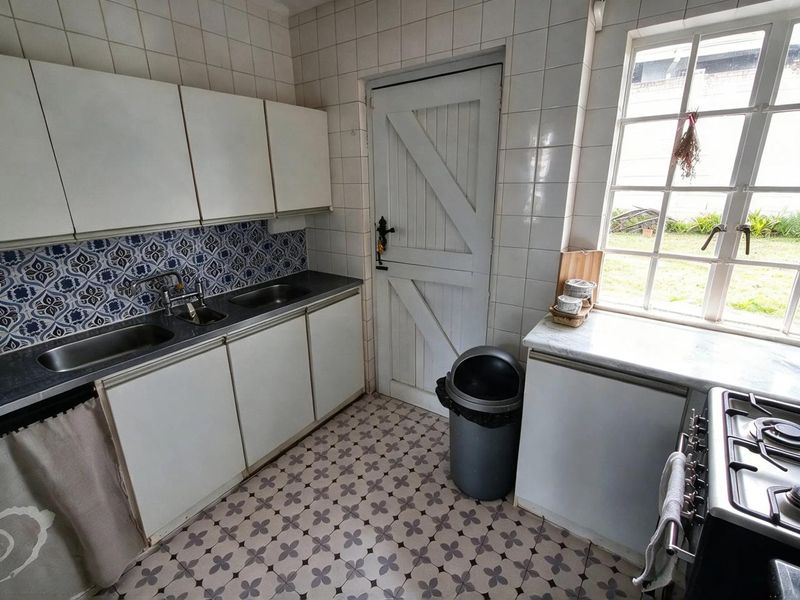 A functional kitchen featuring white cabinetry, patterned tiled flooring, a double sink, and a classic timber door leading to the exterior.
