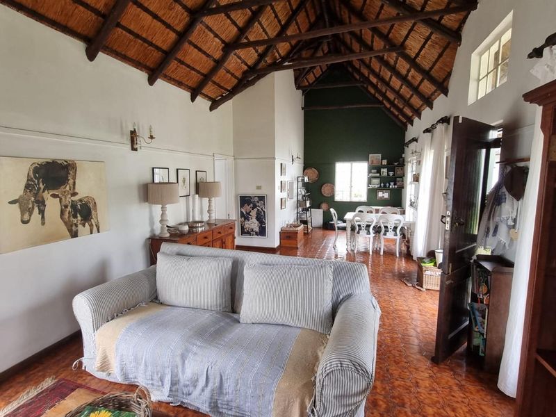 Spacious open-plan living and dining area featuring a high vaulted ceiling with exposed timber rafters, thatched roofing, and traditional terracotta floor tiles.