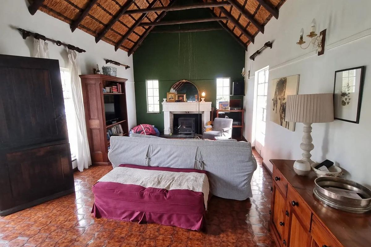 Spacious living room featuring a high vaulted thatched ceiling with exposed timber rafters, a traditional fireplace with a wood-burning stove, and tiled flooring.