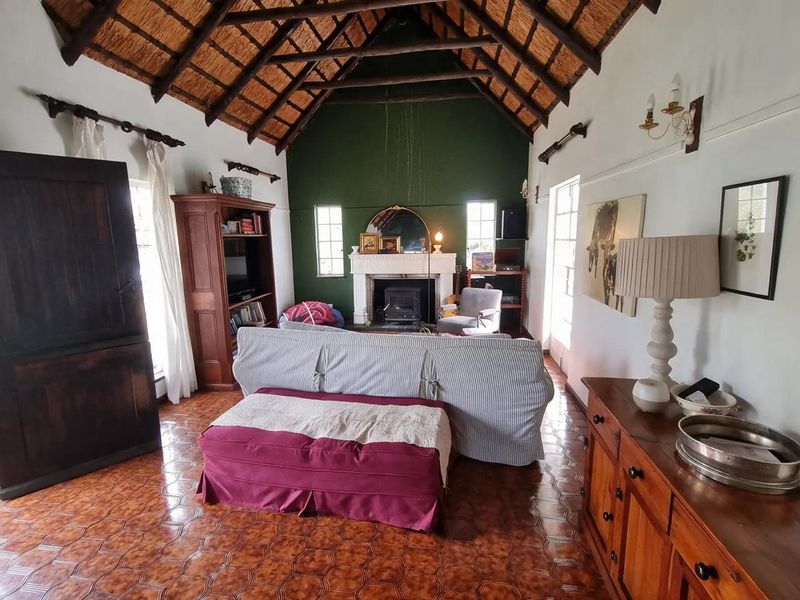 Spacious living room featuring a high vaulted thatched ceiling with exposed timber rafters, a traditional fireplace with a wood-burning stove, and tiled flooring.