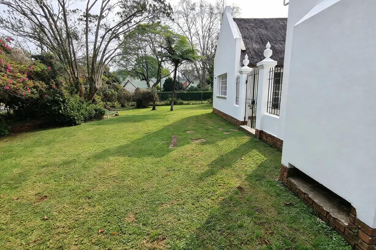 A well-maintained rear garden featuring a white-walled home with a traditional thatched roof and a secure wrought iron gate entrance.
