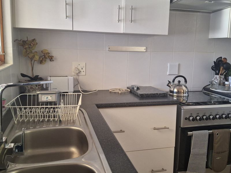 A functional kitchen featuring white cabinetry, dark laminate countertops, a stainless steel double sink, and a freestanding stove with an extractor fan.