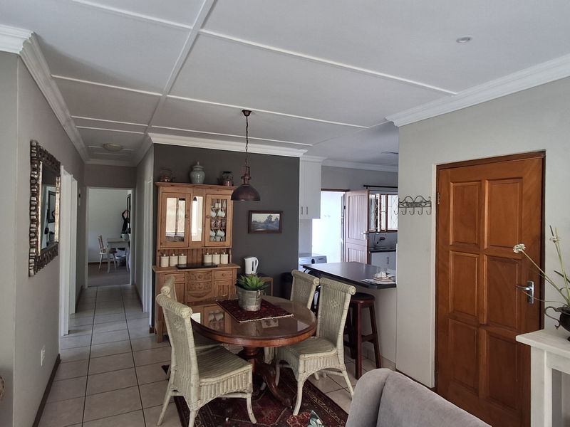 Open plan dining area featuring tiled flooring, crown molding, and a breakfast bar connecting to the kitchen, with access to a hallway.