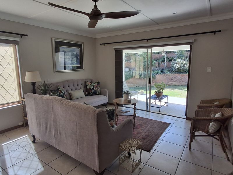 A bright living room featuring tiled flooring, a ceiling fan, and large sliding glass doors that provide direct access to the rear patio and garden.