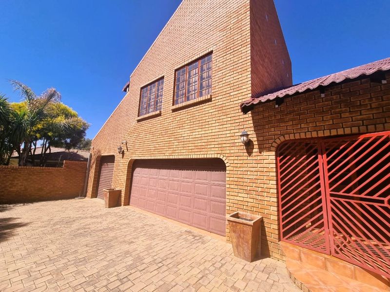 Front elevation of a face brick house featuring a double garage, a single garage, paved driveway, and a secure gated entrance.