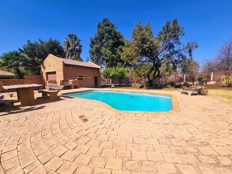 Outdoor pool area featuring a swimming pool, brick paving, and a brick outbuilding with a built-in braai, set within a landscaped garden.