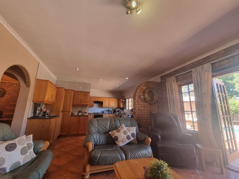 Open-plan living area featuring a kitchen with wooden cabinetry, tiled floors, and an exposed brick feature wall with direct access to the outdoor area.