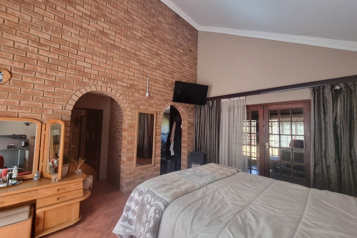 Spacious bedroom featuring an exposed brick wall, vaulted ceilings, arched entryways, and direct access to the outdoors through classic french doors.