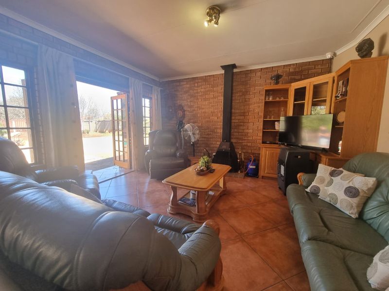 A cozy living room featuring exposed brick walls, tiled flooring, a freestanding fireplace, and direct access to the outdoor area through french doors.