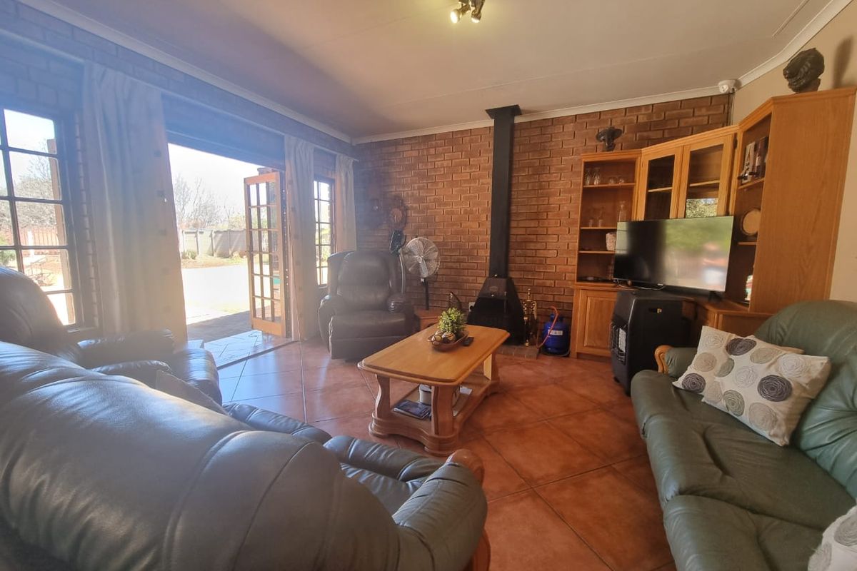 A cozy living room featuring exposed brick walls, tiled flooring, a freestanding fireplace, and direct access to the outdoor area through french doors.